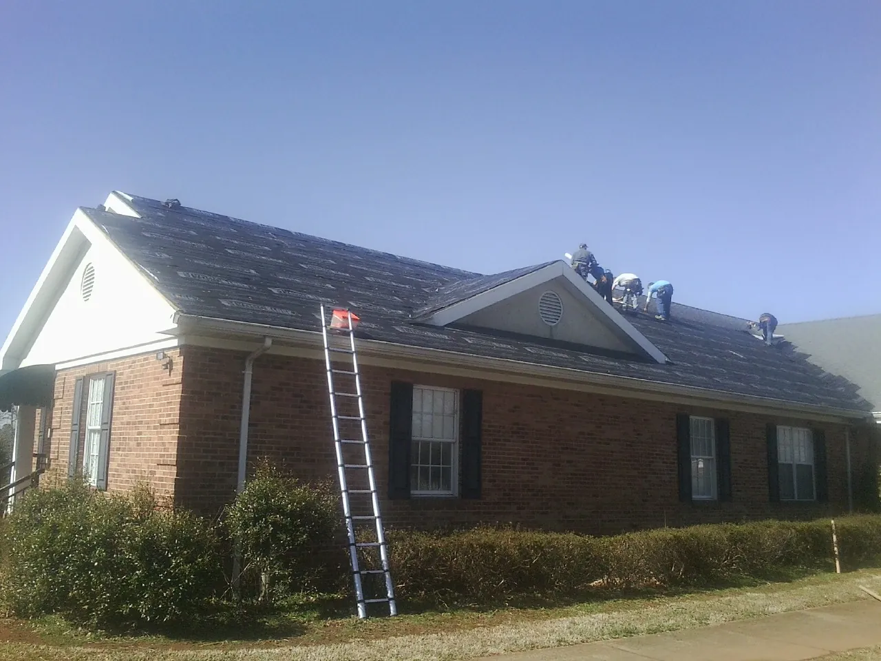 Crew tearing shingles off a brick ranch roof with a ladder set — Emergency Roof Repair work by our crew in West Decatur