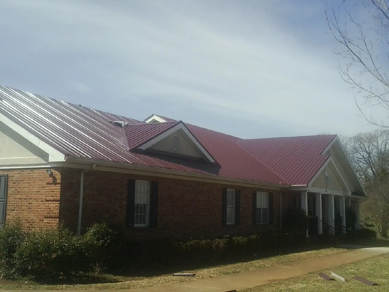 Red metal roof with gabled entries on a long brick building, from a Hail Damage Roof Repair job in West Decatur