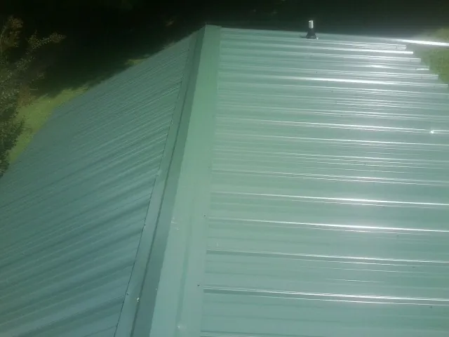 New green metal panels meeting at the ridge of a roof — Flat Roof Repair work by our crew in West Decatur