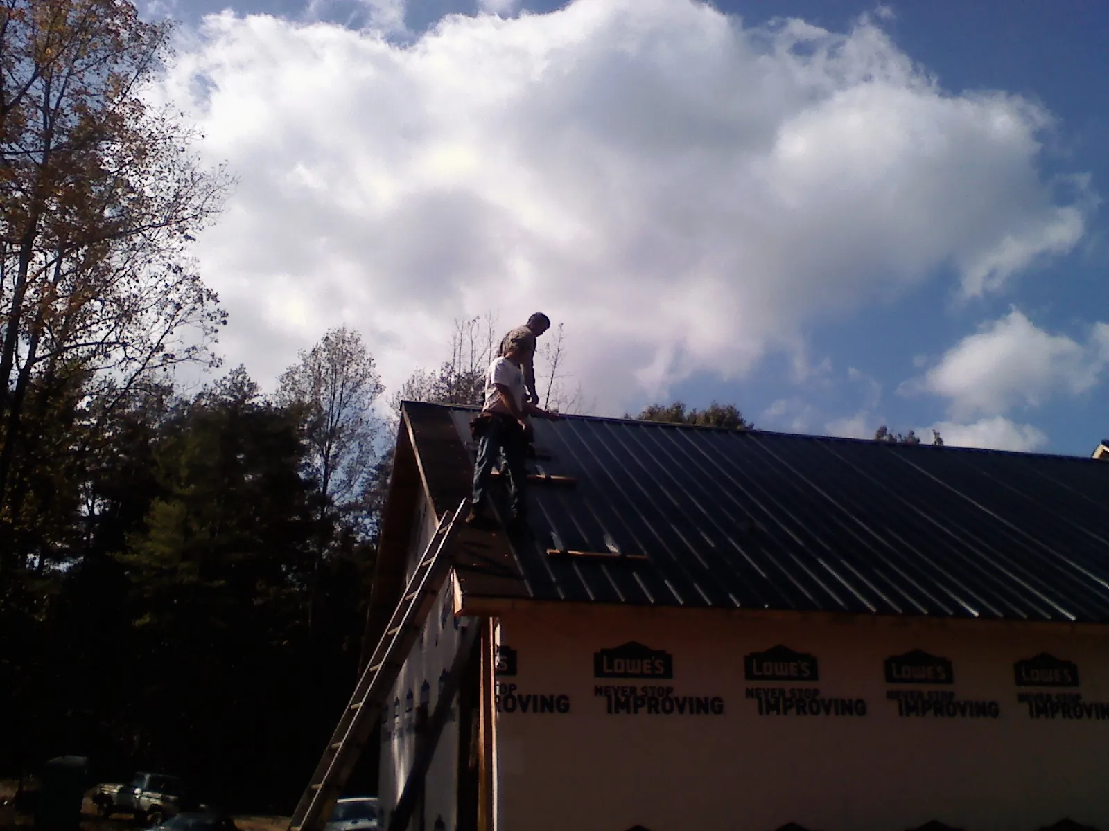Roofer fastening dark metal panels high against a cloudy sky, from a Roof Inspection job in West Decatur