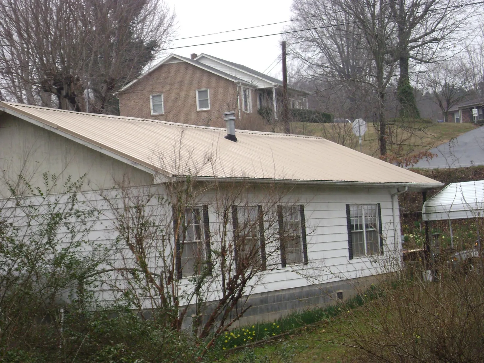 Tan metal roof on a white sided house set into a hillside — Commercial Roofing by Roofing Brothers in West Decatur